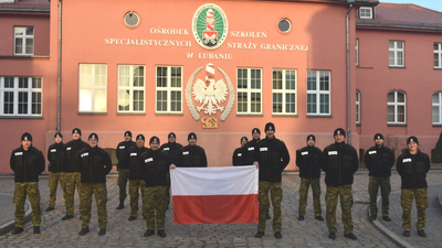 Funkcjonariusze SG stoją i trzymają polską flagę 