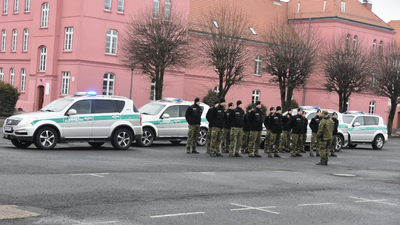 Funkcjonariusze SG stoją w grupie obok samochodów 