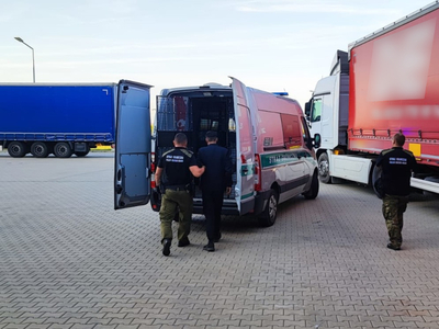 funkcjonariusz SG prowadzący cudzoziemca do auta służbowego 