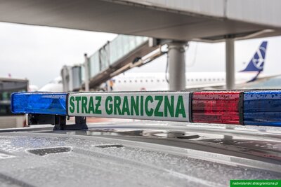 belka sygnalizacyjna na dachu auta z napisem Straż Graniczna, samolot w tle 