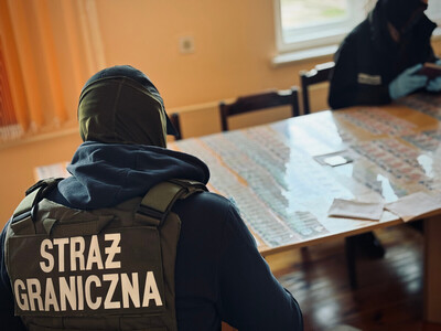 Funkcjonariusz Straży Granicznej przy stole, na którym znajdują się podrobione dokumenty 