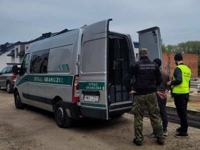 Funkcjonariusze SG prowadzą zatrzymanego cudzoziemca do auta 