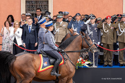 Dwoje funkcjonariuszy Policji jedzie konno w tle uczestnicy Centralnych Obchodów Święta Policji Dwoje funkcjonariuszy Policji jedzie konno w tle uczestnicy Centralnych Obchodów Święta Policji