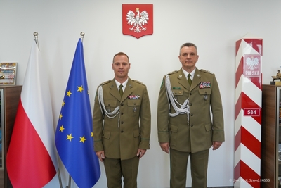 Komendant Główny Straży Granicznej wraz z Komendantem Warmińsko-Mazurskiego Oddziału Straży Granicznej stoją między flagami Polski i Unii Europejskiej, a słupem granicznym Komendant Główny Straży Granicznej wraz z Komendantem Warmińsko-Mazurskiego Oddziału Straży Granicznej stoją między flagami Polski i Unii Europejskiej, a słupem granicznym