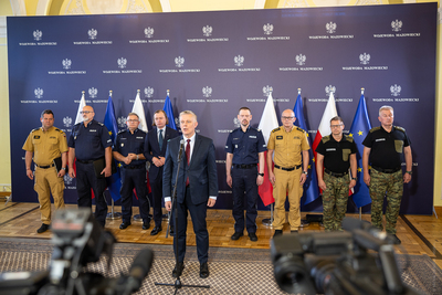 Minister SWiA przemawia, w tle stoją szefowie służb Minister SWiA przemawia, w tle stoją szefowie służb