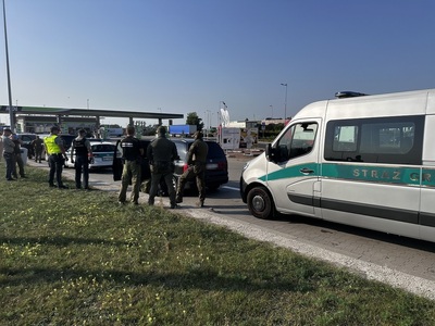 Funkcjonariusze Straży Granicznej i Krajowej Administracji Skarbowej przy zatrzymanym pojeździe z cudzoziemcami, na pierwszym planie pojazd SG Funkcjonariusze Straży Granicznej i Krajowej Administracji Skarbowej przy zatrzymanym pojeździe z cudzoziemcami, na pierwszym planie pojazd SG
