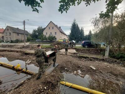 Funkcjonariusze Straży Granicznej niosą przedmiot przez rów z wodą Funkcjonariusze Straży Granicznej niosą przedmiot przez rów z wodą
