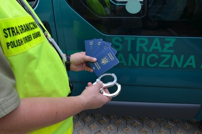 Funkcjonariusz Straży Granicznej trzyma ukraińskie paszporty i kajdanki Funkcjonariusz Straży Granicznej trzyma ukraińskie paszporty i kajdanki
