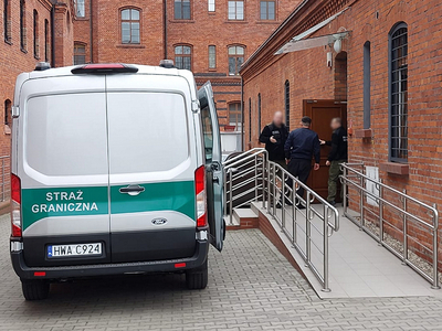 Pojazd Straży Granicznej obok funkcjonariusze SG z zatrzymanymi Pojazd Straży Granicznej obok funkcjonariusze SG z zatrzymanymi