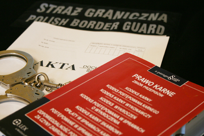 Kodeks karny i kajdanki akta sprawy leżą na kamizelce z napisem Straż Graniczna Kodeks karny i kajdanki akta sprawy leżą na kamizelce z napisem Straż Graniczna